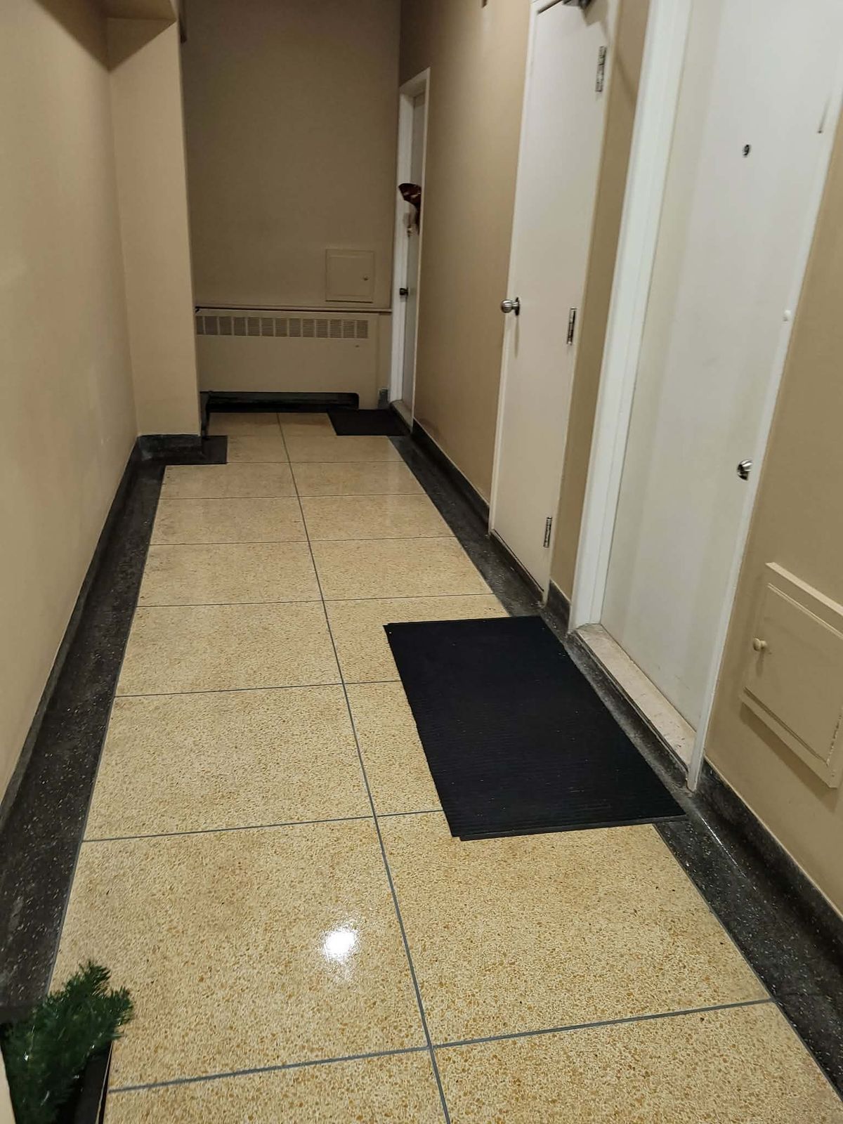 Corridor d'immeuble résidentiel, plancher de terrazzo lavé et tapis d'entrée noirs devant les portes d'appartement
